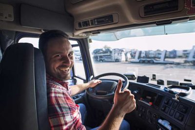 Smiling truck driver on drivers seat, trucking insurance